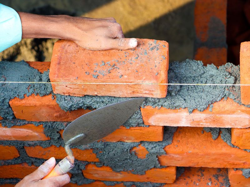 Hands laying a brick to a string line with a trowel