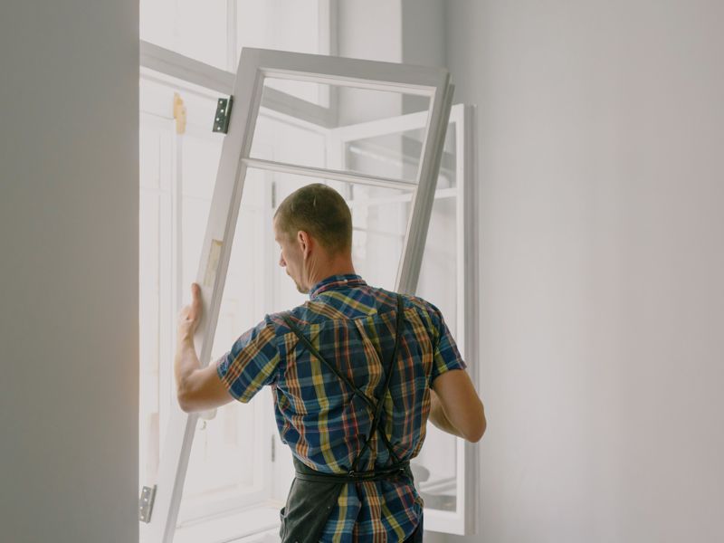 A builder carrying a window frame on site