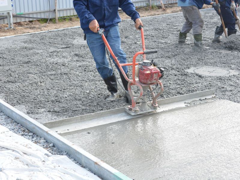 A worker screeding a freshly poured concrete slab