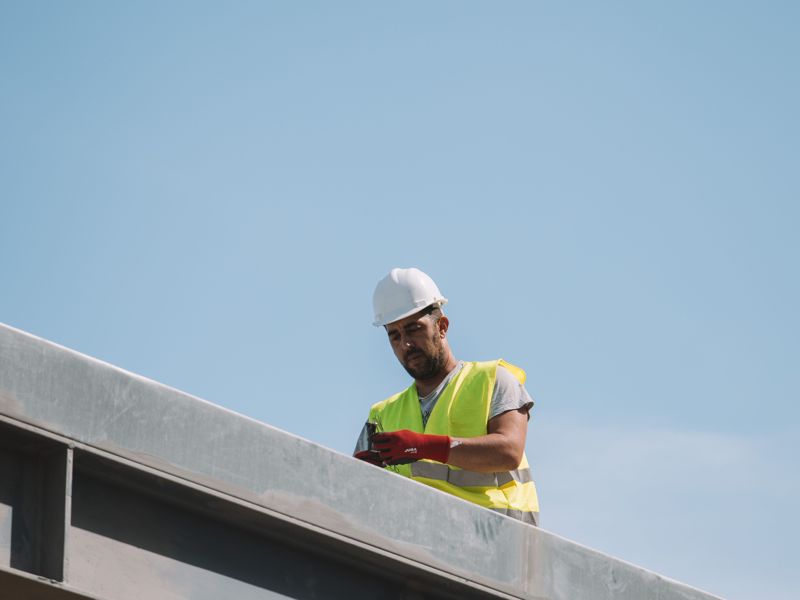 A construction worker in a hard hat on a steel roof frame