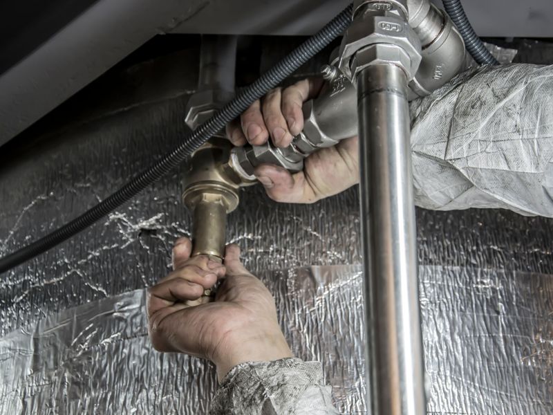 Hands fitting steel pipework under an insulated floor