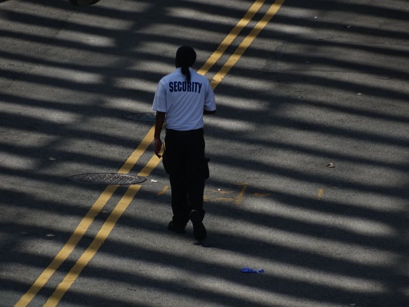 A security guard walking across a sunlit street, seen from above