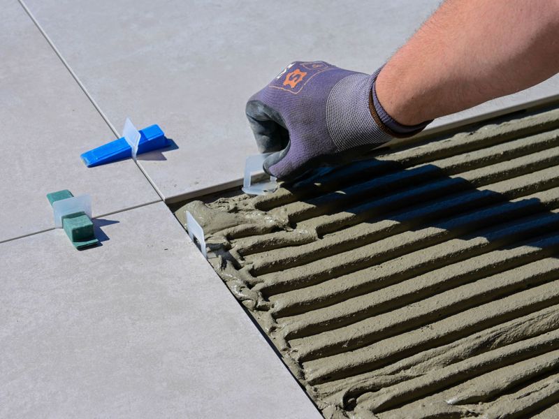 A gloved hand setting floor tiles with levelling spacers