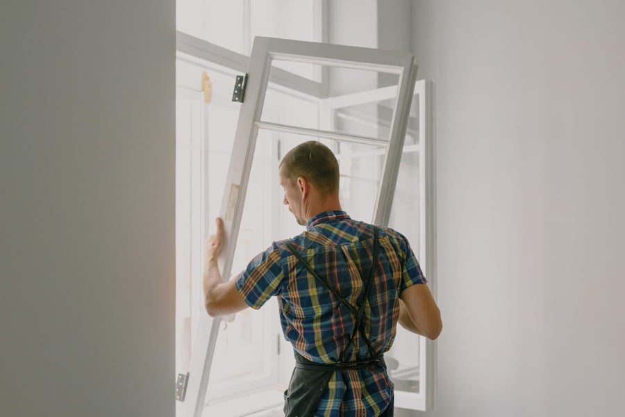 A carpenter carrying a window frame through a room being renovated
