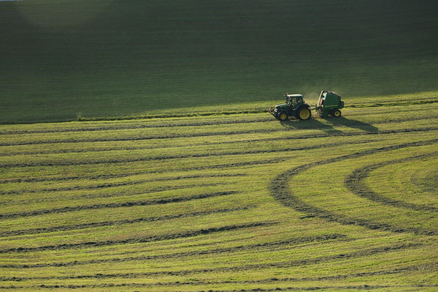 A tractor and baler working a field in late afternoon light